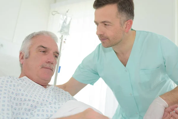 Mannelijke verpleegkundige helpen senior patiënt op bed — Stockfoto