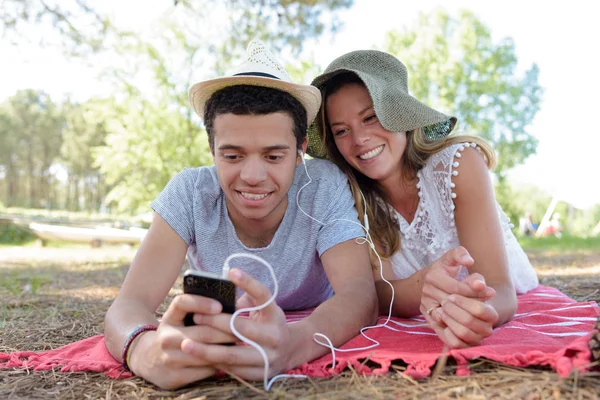 Молодая пара, лежащая в парке и слушающая музыку — стоковое фото