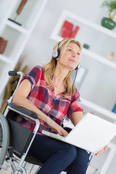 ノートパソコンやヘッドフォンを備えた車椅子の障害者女性は — ストック写真