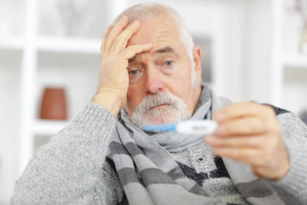 Старший мужчина проверяет температуру тела с помощью термометра — стоковое фото