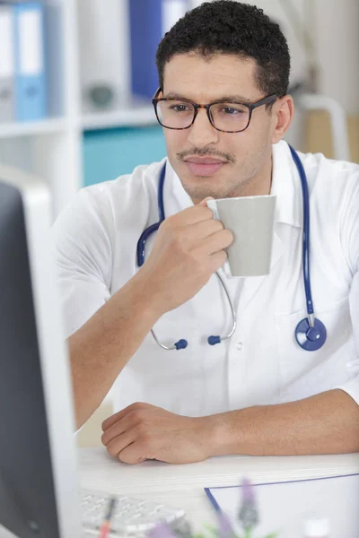 Giovane medico con tazza di caffè nello studio medico — Foto Stock