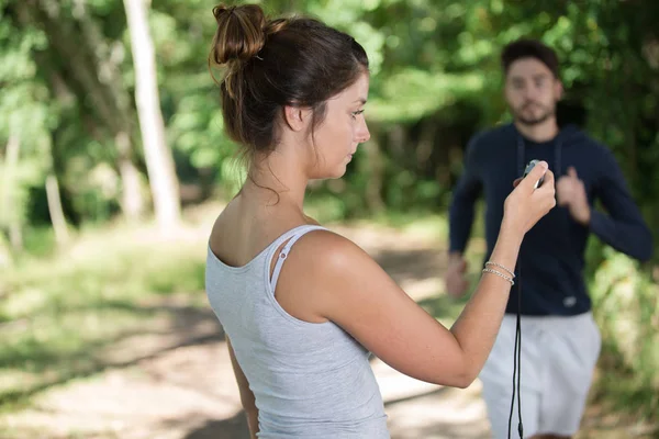 Porträtt av kvinnliga coach timing löpare i en park — Stockfoto