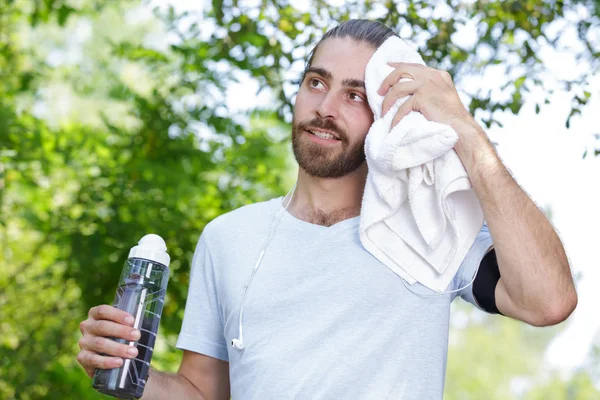 Hombre sosteniendo una botella de agua y limpiándose la frente con una toalla —  Fotos de Stock