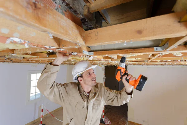 Handwerksman met boor op houten frame voor plafond — Stockfoto