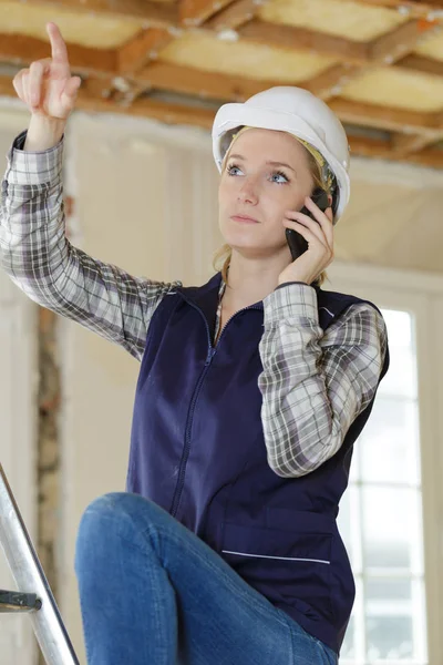 Mulher construtor no telefone apontando para a reparação — Fotografia de Stock