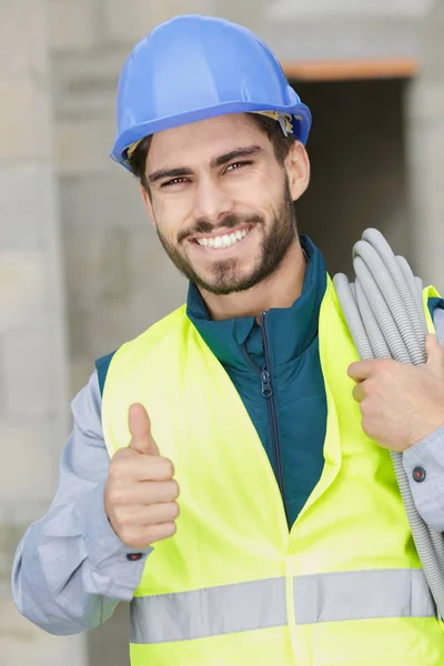 Constructor alegre con cable eléctrico que muestra el pulgar hacia arriba —  Fotos de Stock