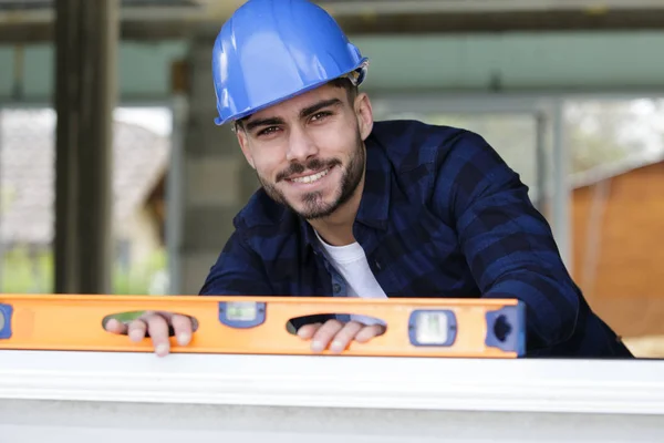 Joven reparador sosteniendo un nivel de espíritu sonriendo a la cámara — Foto de Stock