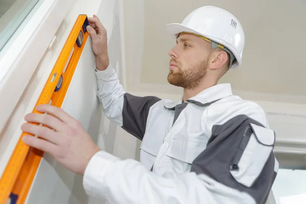 Hombre joven constructor en la construcción de casco celebración de nivel de espíritu —  Fotos de Stock