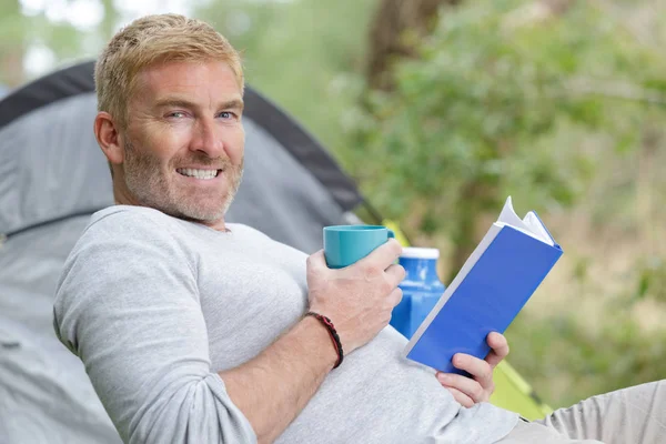 Camper reading a book seated on the ground — Stock Photo, Image