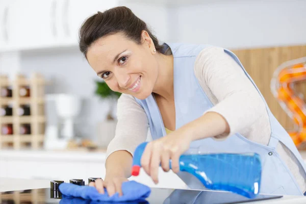 Mujer feliz limpieza paño de cocina y spray en la cocina —  Fotos de Stock