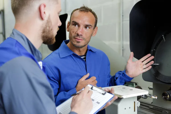 Two workers wearing protective uniform talking in factory — Stock Photo, Image