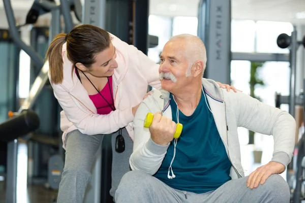 女子教练在健身中心训练有哑铃的老年男子 — 图库照片