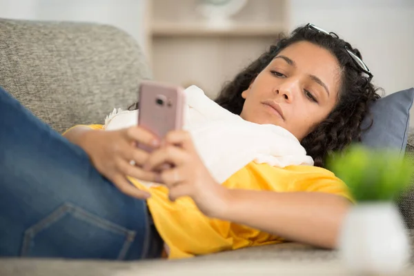 女人躺在沙发上玩手机游戏 — 图库照片