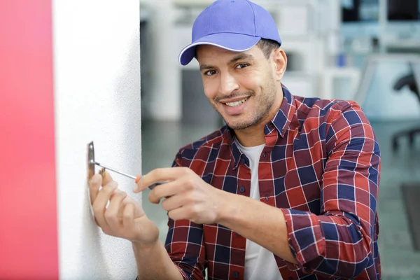 service man installing power socket in wall with screwdriver