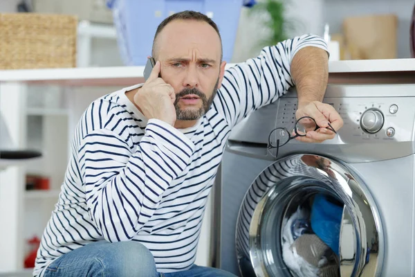 man making telephone call crouched beside washing machine