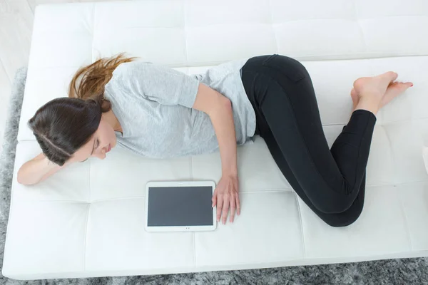 young lady on futon with tablet showing blank screen