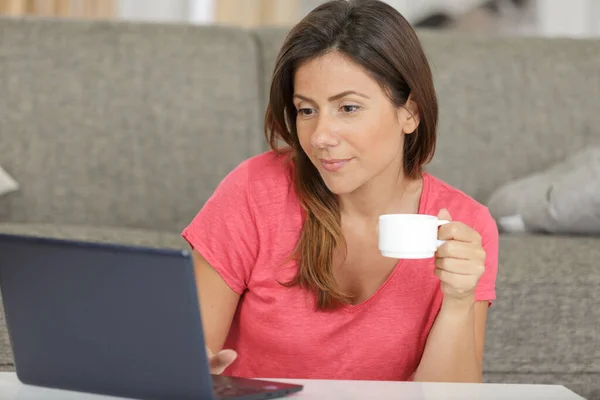 妇女在客厅里喝咖啡时使用笔记本电脑 — 图库照片