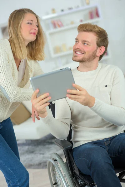 坐在轮椅上的男人和他的女朋友一起用平板电脑 — 图库照片