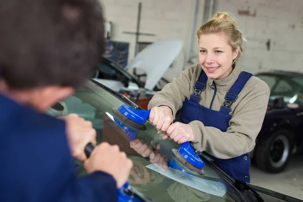 female mechanic is changing windscreen on car