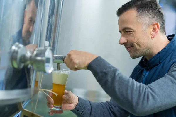 brewer filling glass of beer from vat