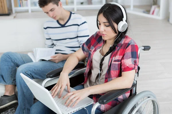 Jovem Menino Leitura Livro Jovem Senhora Cadeira Rodas Usando Laptop — Fotografia de Stock