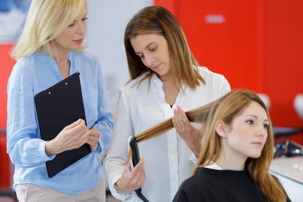 ヘアアイロンでロングヘアを矯正する訓練生の美容師 — ストック写真