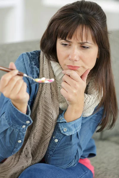 不确定的女人拿着勺子吃药 — 图库照片