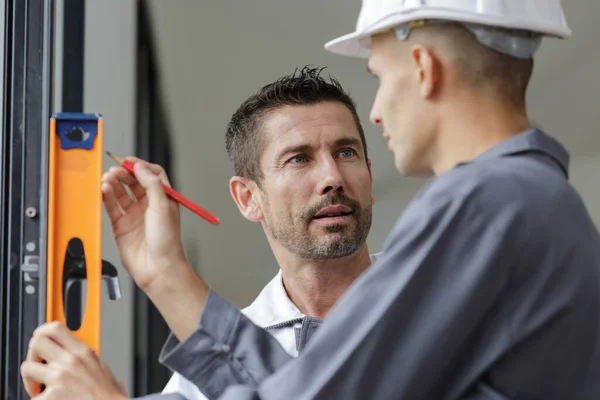 Zwei Bauarbeiter Reden Während Sie Wasserwaage Gegen Fenster Halten — Stockfoto