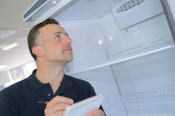 Πολυτεχνίτης Στέκεται Κοντά Στο Ψυγείο Και Κρατώντας Σημειώσεις — Φωτογραφία Αρχείου