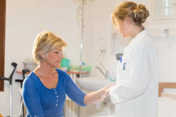 病院の部屋で高齢女性患者の腕を調べる医師 — ストック写真
