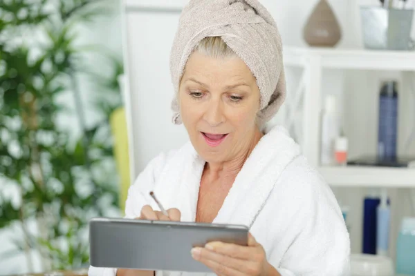 笑着拿浴巾检查平板电脑的女人 — 图库照片