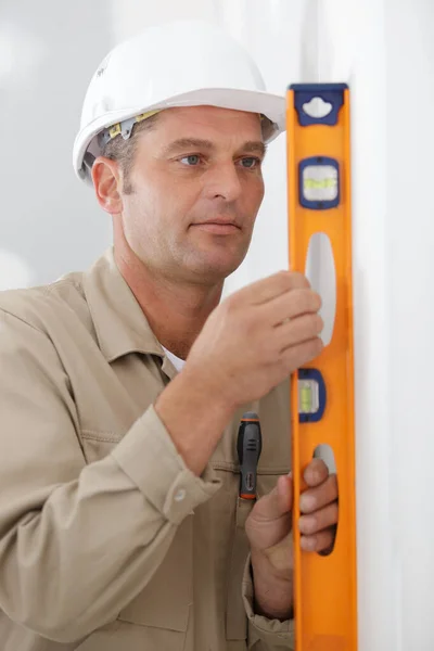 戴头盔的建筑工人正在测量有水平的墙 — 图库照片
