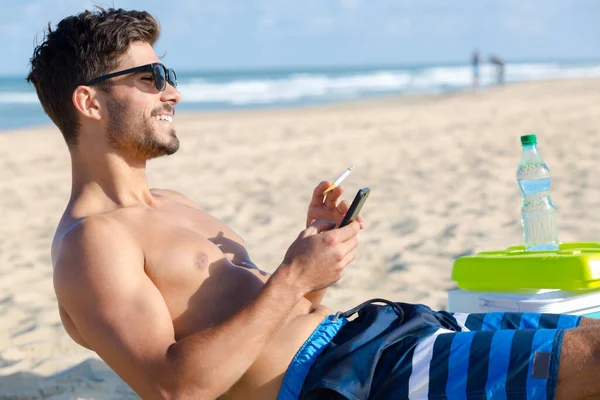 Junger Mann Raucht Und Benutzt Sein Handy Strand — Stockfoto