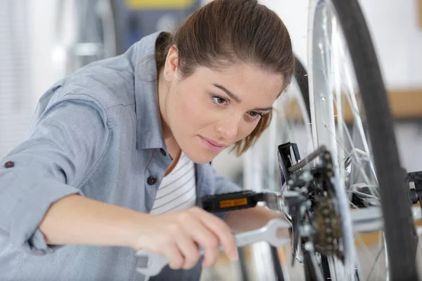 若い幸せな正の女性のマスターはワークショップで自転車を修理しています — ストック写真