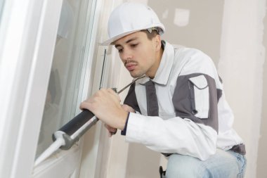 young contractor applying sealer around window frame clipart