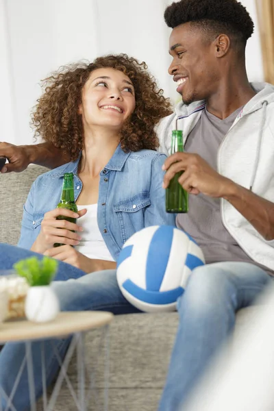快乐的年轻夫妇坐在沙发上喝啤酒 — 图库照片
