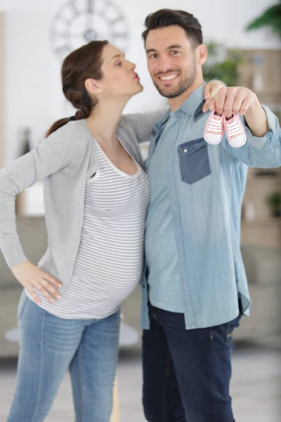 Picture Showing Happy Couple Kissing While Holding Baby Shoes — Stock Photo, Image