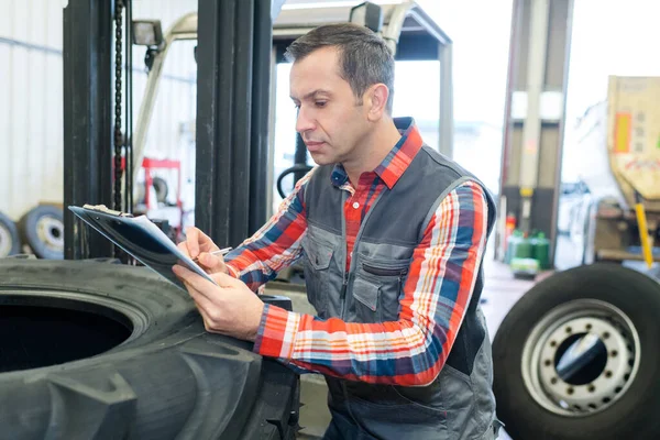 Mechaniker Stützt Sich Auf Reifen Auf Klemmbrett Schreiben — Stockfoto