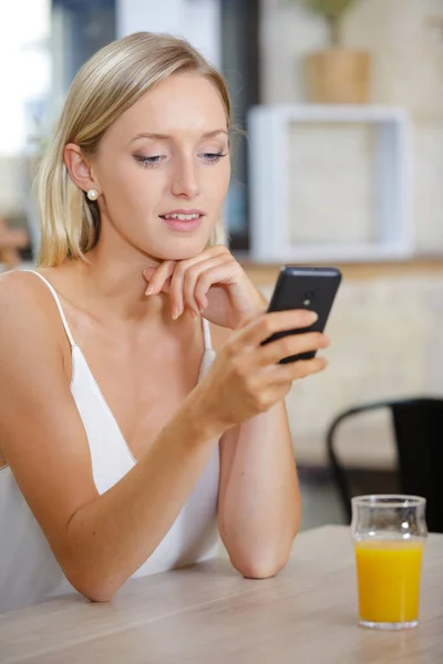 年轻女人在酒吧里用橙汁发短信 — 图库照片