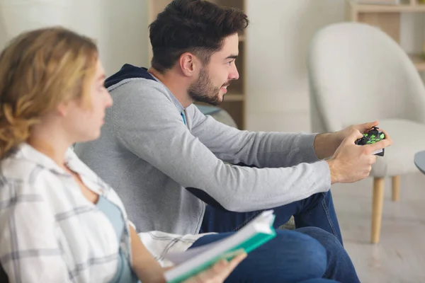 Frau Liest Während Ihr Partner Ein Computerspiel Spielt — Stockfoto