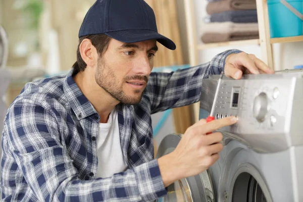 working man plumber repairs a washing machine in laundry