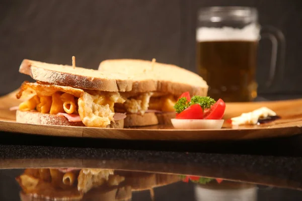 Sanduíches em uma chapa de madeira com uma cerveja na mesa — Fotografia de Stock