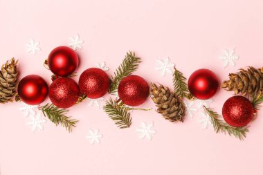 Kırmızı Noel parlak topları ve soluk pembe arka planda köknar dalları. Noel süsleri düzenleme.