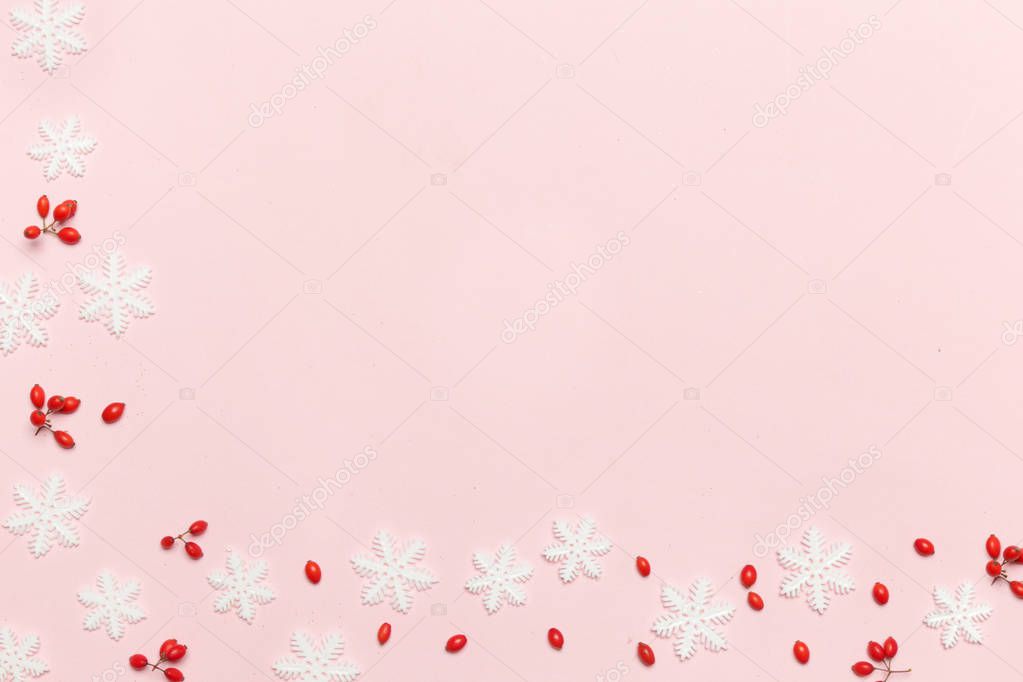 Elegant winter background with copy space. Red berries and snow flakes on pale pink background. Christmas, winter holiday, new year concept.