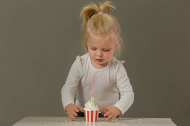 Küçük bir kızın bir kekten doğum günü mumu üflerken çekilmiş bir fotoğrafı.