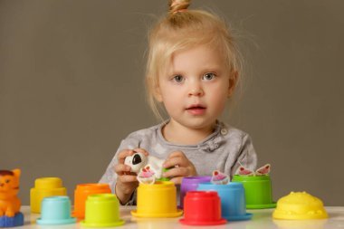 Renkli plastik bardaklarla oynayan bir çocuğun stüdyo fotoğrafı, motor beceri geliştirme. Yeni yürümeye başlayanlar için bu aktiviteler küçük elleri ve parmakları daha sonraki gelişim becerileri için hazırlayacak..