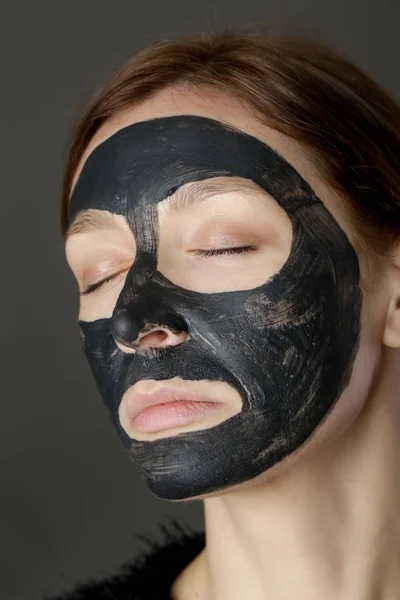 Charcoal face mask or black clay mud. Beautiful woman with black mask on her face, close up studio head shot. Natural cosmetic concept.