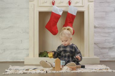 Evinde kırmızı Noel çoraplarıyla süslenmiş ahşap şöminenin önünde oynayan sevimli bir kız.