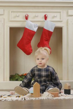 Evinde kırmızı Noel çoraplarıyla süslenmiş ahşap şöminenin önünde oynayan sevimli bir kız.