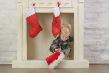 Evinde kırmızı Noel çoraplarıyla süslenmiş ahşap şöminenin önünde oynayan sevimli bir kız.